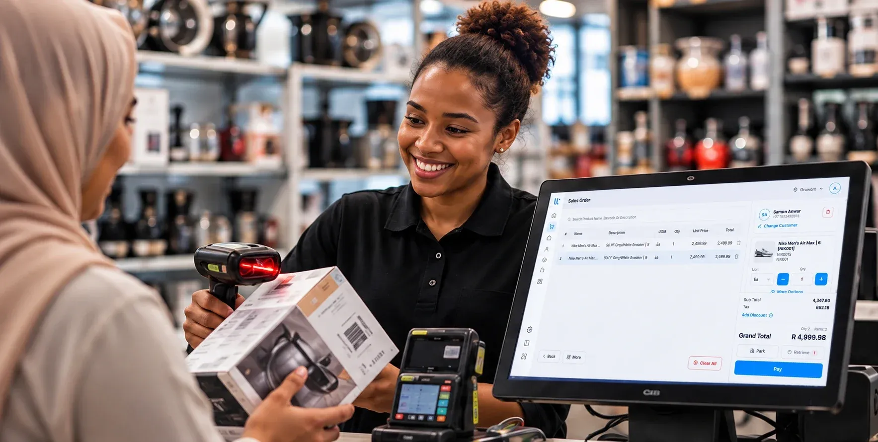 A shop assistant scans a boxed kettle with a barcode scanner while the till screen shows the order total in rands